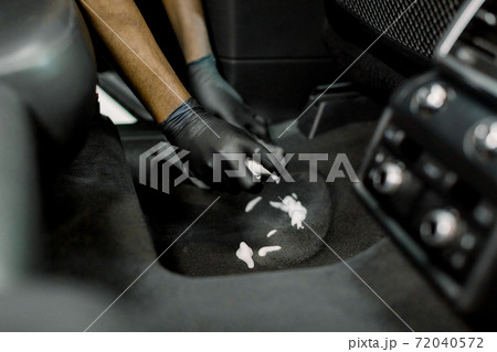 Cropped close up of hands of professional male detailer in black gloves, cleaning the carpet of car interior, applying disinfecting cleaning foam Cropped close up of hands of professional male detailer in black gloves, cleaning the carpet of car interior, applying disinfecting cleaning foam 72040572