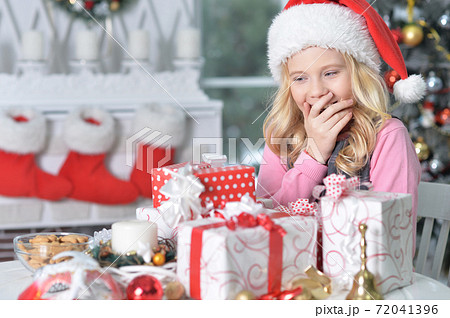 Happy girl in Santa hat sitting with Christmas presents 72041396