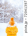 Back view of young woman wearing yellow jacket walks in snowy park 72041397
