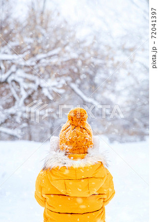 Back view of young woman wearing yellow jacket walks in snowy park 72041397