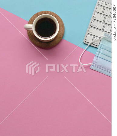 Cup of coffee next to face mask and keyboard on top of pink and blue tabletop. 72046007