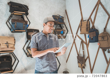 asian male business owner in a bag shop with tablet asian male business owner in a bag shop with tablet 72047863