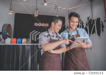 coffee shop owner discussing with his employee using tablet 72049153