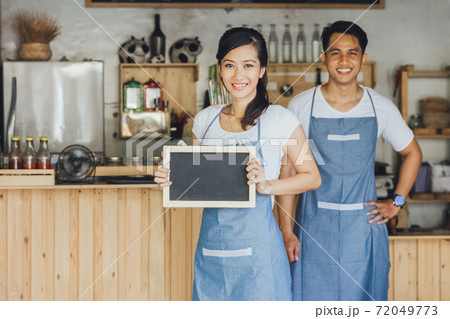 young female waitress standing and holding blank blackboard sign at a cafe 72049773