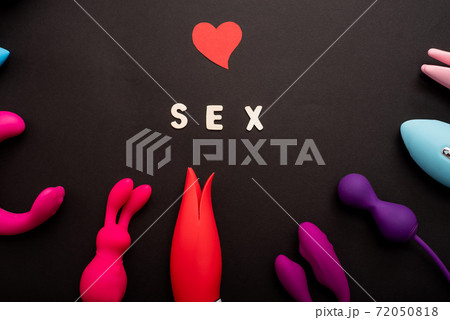The inscription sex heart and a collection of multicolored vibrators on a black background. Sex toys of various shapes. Assortment of sex shop The inscription sex heart and a collection of multicolored vibrators on a black background. Sex toys of various shapes. Assortment of sex shop 72050818