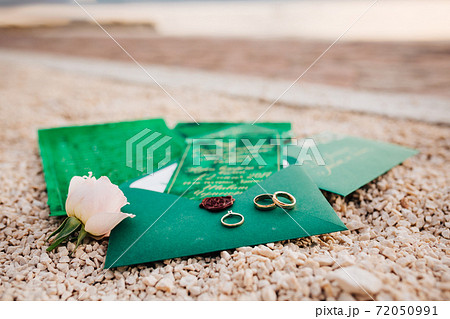Gold wedding rings for the bride and groom on a green envelope with invitations on decorative stones. Gold wedding rings for the bride and groom on a green envelope with invitations on decorative stones. 72050991