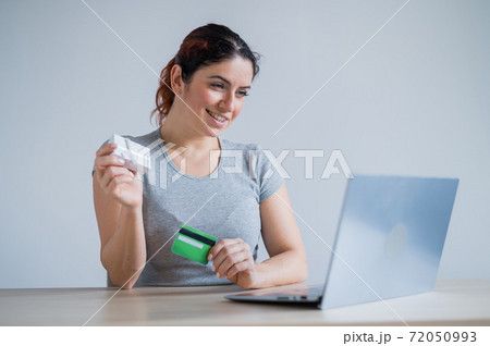 Caucasian woman holding a gift box and a credit card while sitting at a laptop. The girl buys gifts online Caucasian woman holding a gift box and a credit card while sitting at a laptop. The girl buys gifts online 72050993