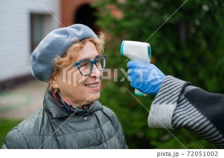 The doctor measures the temperature of an elderly woman with a non-contact infrared thermometer outdoors The doctor measures the temperature of an elderly woman with a non-contact infrared thermometer outdoors 72051002