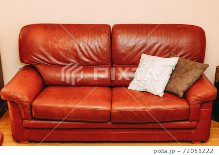 Folding sofa made of burgundy genuine leather with white and brown pillows in the room. 72051222