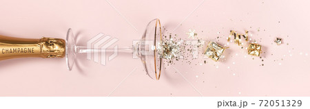 Bottle of champagne, glass with splash of confetti and golden decorations over pink background 72051329