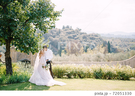 Wedding in Florence, Italy, in an old villa-winery. Bride and groom in the shade of a tree. Wedding couple walks in the garden. 72051330