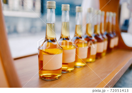 Bottles with a golden alcoholic beverage. Empty labels. Bottles of Rakia are on display in a row. Bottles with a golden alcoholic beverage. Empty labels. Bottles of Rakia are on display in a row. 72051413