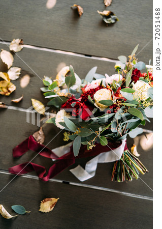 bridal bouquet of white and red roses, peonies, branches of eucalypt tree, alstroemeria and chrysantemum, red berries with white and maroon ribbons, on the table  72051488