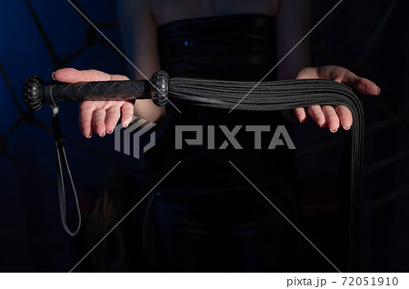 Black leather lash in the hands of an unrecognizable woman. Cropped photo of bdsms toys. Punishment and pleasure. Black leather lash in the hands of an unrecognizable woman. Cropped photo of bdsms toys. Punishment and pleasure. 72051910