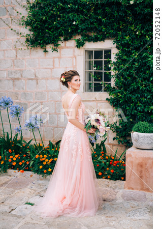 beautiful bride in tender wedding dress with bridal bouquet near window of old house in Perast 72052148