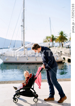 Father is pushing his daughter in a pink stroller  72052193