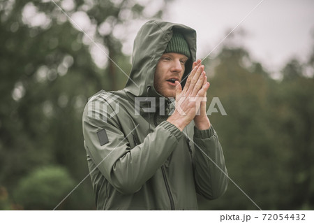 Young man in a green coat standing in the rain 72054432