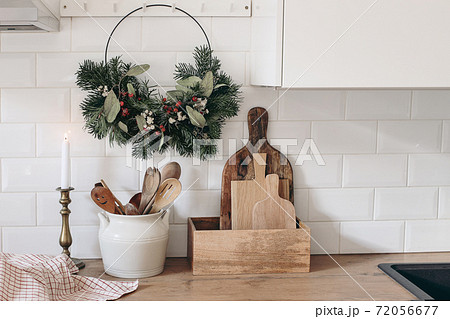 Closeup of kitchen interior. Christmas decoration. Advent floral hoop wreath hanging on peg rails. White brick wall, metro tiles, wooden countertops with kitchen utensils. Vintage scandinavian design. Closeup of kitchen interior. Christmas decoration. Advent floral hoop wreath hanging on peg rails. White brick wall, metro tiles, wooden countertops with kitchen utensils. Vintage scandinavian design. 72056677