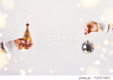 Female hands in white sweater holding golden Christmas tree and mirror disco ball on white background, copy space Female hands in white sweater holding golden Christmas tree and mirror disco ball on white background, copy space 72057061