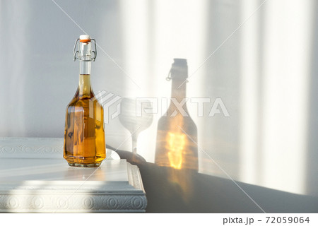 Elegant bottle with alcohol and empty glass over a vintage cabinet and a beautiful sun reflection on the wall - art concept Elegant bottle with alcohol and empty glass over a vintage cabinet and a beautiful sun reflection on the wall - art concept 72059064