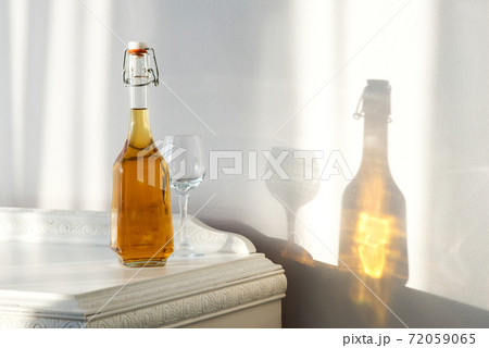 Elegant bottle with alcohol and empty glass over a vintage cabinet and a beautiful sun reflection on the wall - art concept Elegant bottle with alcohol and empty glass over a vintage cabinet and a beautiful sun reflection on the wall - art concept 72059065
