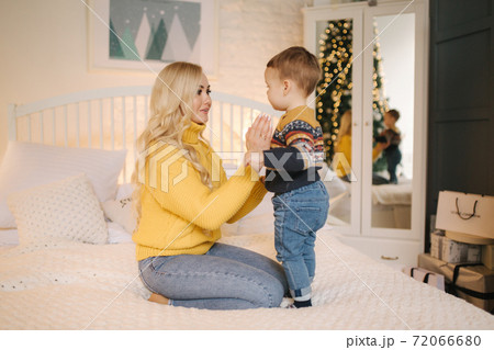 Portrait of mom and son sitting on a bed at home near the Christmas tree, all are smiling. Christmas family. Happiness 72066680