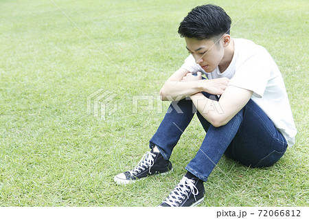 芝生に座り俯く若い男性横顔 72066812