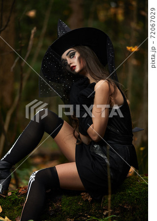 Young woman in black dress with witch hat and orange pumpkin placed around in the forest, Halloween concept. Horror theme. Young woman in black dress with witch hat and orange pumpkin placed around in the forest, Halloween concept. Horror theme. 72067029