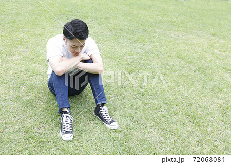 芝生に座り俯く若い男性横顔 72068084