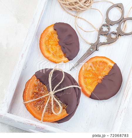 Candied sliced oranges covered with chocolate on a white tray, top view, square format Candied sliced oranges covered with chocolate on a white tray, top view, square format 72068783