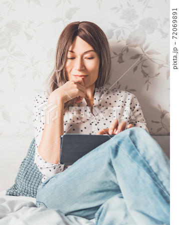 Woman sits on bed with tablet PC. She watches online TV series. Online video call or conference, distance learning, remote education. Self isolation during quarantine. Woman sits on bed with tablet PC. She watches online TV series. Online video call or conference, distance learning, remote education. Self isolation during quarantine. 72069891