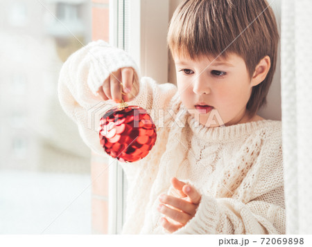 Kid with red decorative ball for Christmas tree. Boy in cable-knit oversized sweater. Cozy outfit for snuggle weather. Winter holiday spirit. New year. Kid with red decorative ball for Christmas tree. Boy in cable-knit oversized sweater. Cozy outfit for snuggle weather. Winter holiday spirit. New year. 72069898