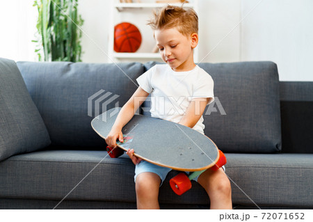 Little boy sitting on sofa at home and holding skateboard 72071652