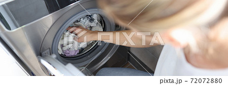Woman folds clothes into the washing machine. Woman folds clothes into the washing machine. 72072880