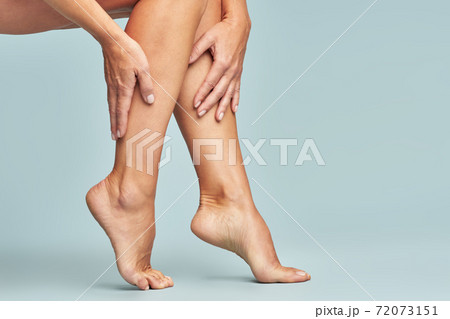 Cropped shot of a woman touching her legs with smooth, silky and soft skin after making a depilation, sitting over blue background 72073151