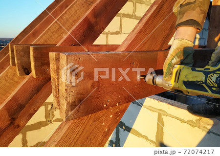The worker uses a drill in the construction of the roof 72074217
