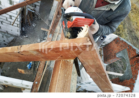 The builder saws on the roof of the chainsaw. Roof rafters. 72074328