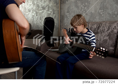 Young male musician teaches little boy student how to play the acoustic guitar and play by notes 72077224