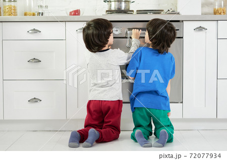 Keep calm. Rear view of curious little hispanic boys, twins watching cake baking in the oven, crouching down in the kitchen 72077934