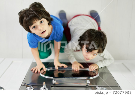 Top view of curious little latin boys, twins looking at camera while sitting in the kitchen and watching pie baking in the oven 72077935