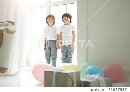 Lovely twins. Two cute latin twin boys, little children in casual wear looking happy, greeting their parents, preparing colorful balloons and giftboxes for them 72077937