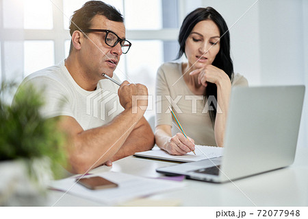 Learning at your own convenience. Middle aged latin couple, man and woman making notes during online training course while studying remotely, using laptop at home Learning at your own convenience. Middle aged latin couple, man and woman making notes during online training course while studying remotely, using laptop at home 72077948
