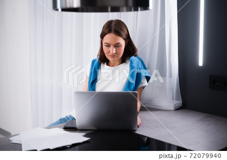 Focused young woman working on small business start up with a laptop. She is sitting at her kitchen table at home 72079940