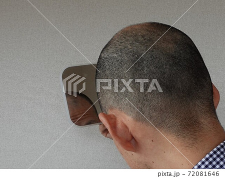 薄毛の悩み 鏡で確認する坊主頭の中年男性の写真素材