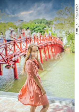 Caucasian woman traveler on background of Red Bridge in public park garden with trees and reflection in the middle of Hoan Kiem Lake in Downtown Hanoi. Vietnam reopens after coronavirus quarantine 72083692
