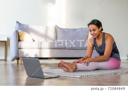 Stretching at home online. African American woman exercising at home in front of a laptop monitor. Stretching at home online. African American woman exercising at home in front of a laptop monitor. 72084849