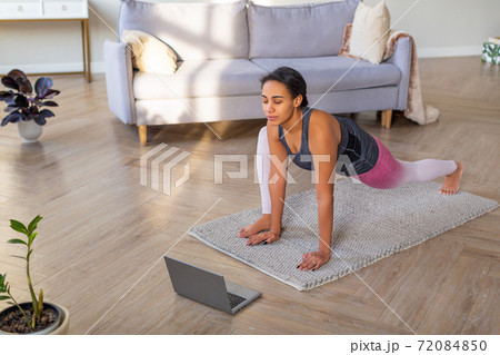 Stretching at home online. African American woman exercising at home in front of a laptop monitor. Stretching at home online. African American woman exercising at home in front of a laptop monitor. 72084850