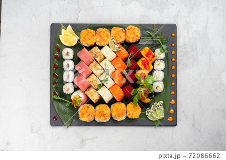 Big beautiful set of different types of sushi maki on a black rectangular stone slate plate. A traditional Japanese dish of raw fish and seafood wrapped in boiled rice and nori seaweed. Big beautiful set of different types of sushi maki on a black rectangular stone slate plate. A traditional Japanese dish of raw fish and seafood wrapped in boiled rice and nori seaweed. 72086662