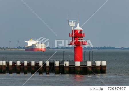Red lighthouse with cargo ship in background, Brunsbuettel, Schleswig-Holstein, North Sea, Germany 72087497