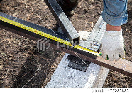 A worker measures metal at a construction site. Technology A worker measures metal at a construction site. Technology 72089889